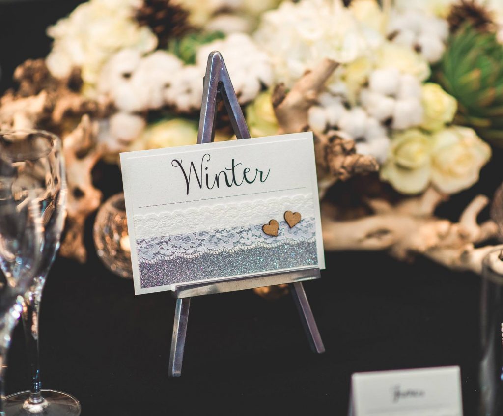 table name decorated with silver glitter lace wooden hearts displayed on small metal easel