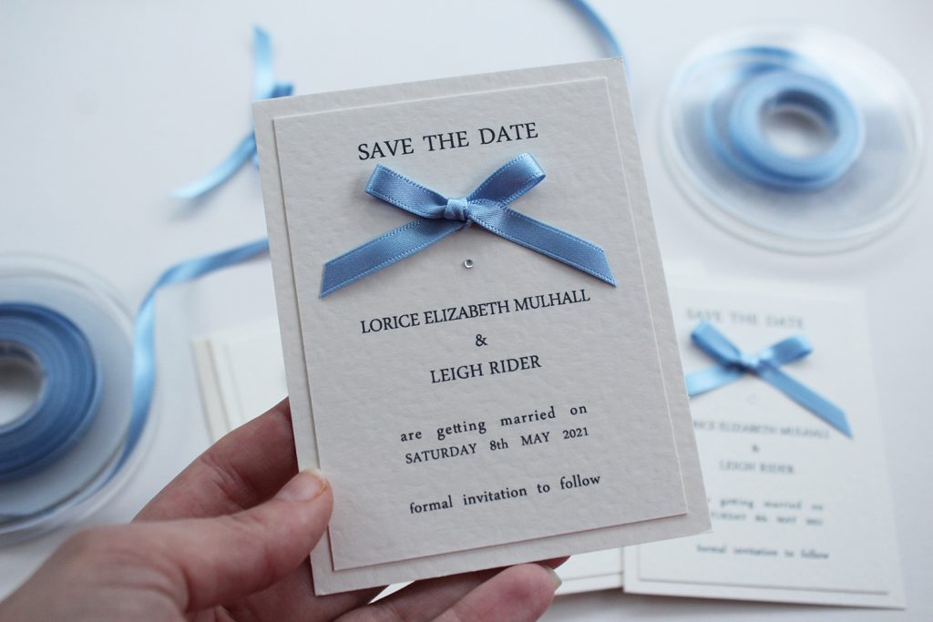 wedding save the dates ivory card blue ribbon bow hand held faded background